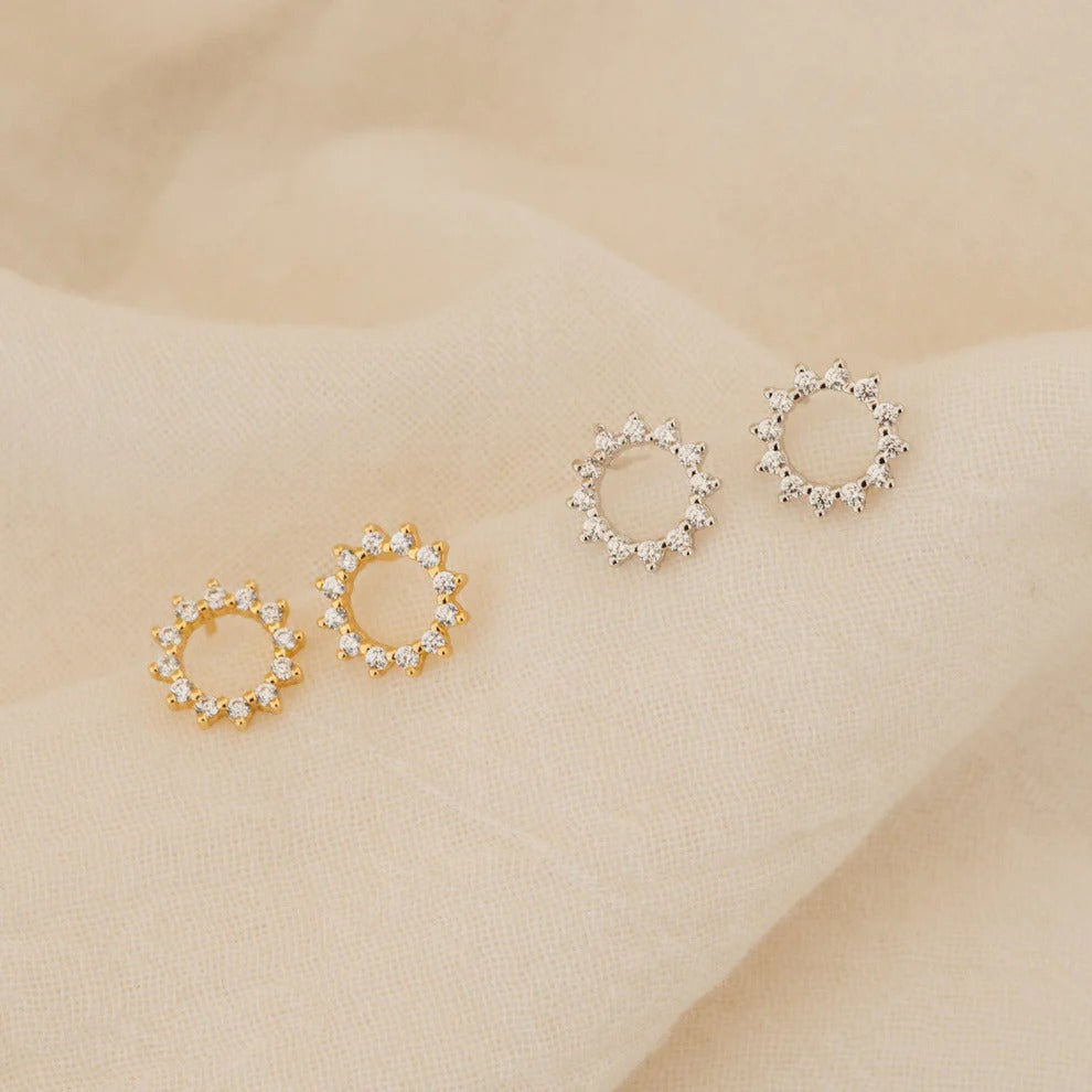 Pair of gold and silver circular earrings on a beige fabric background