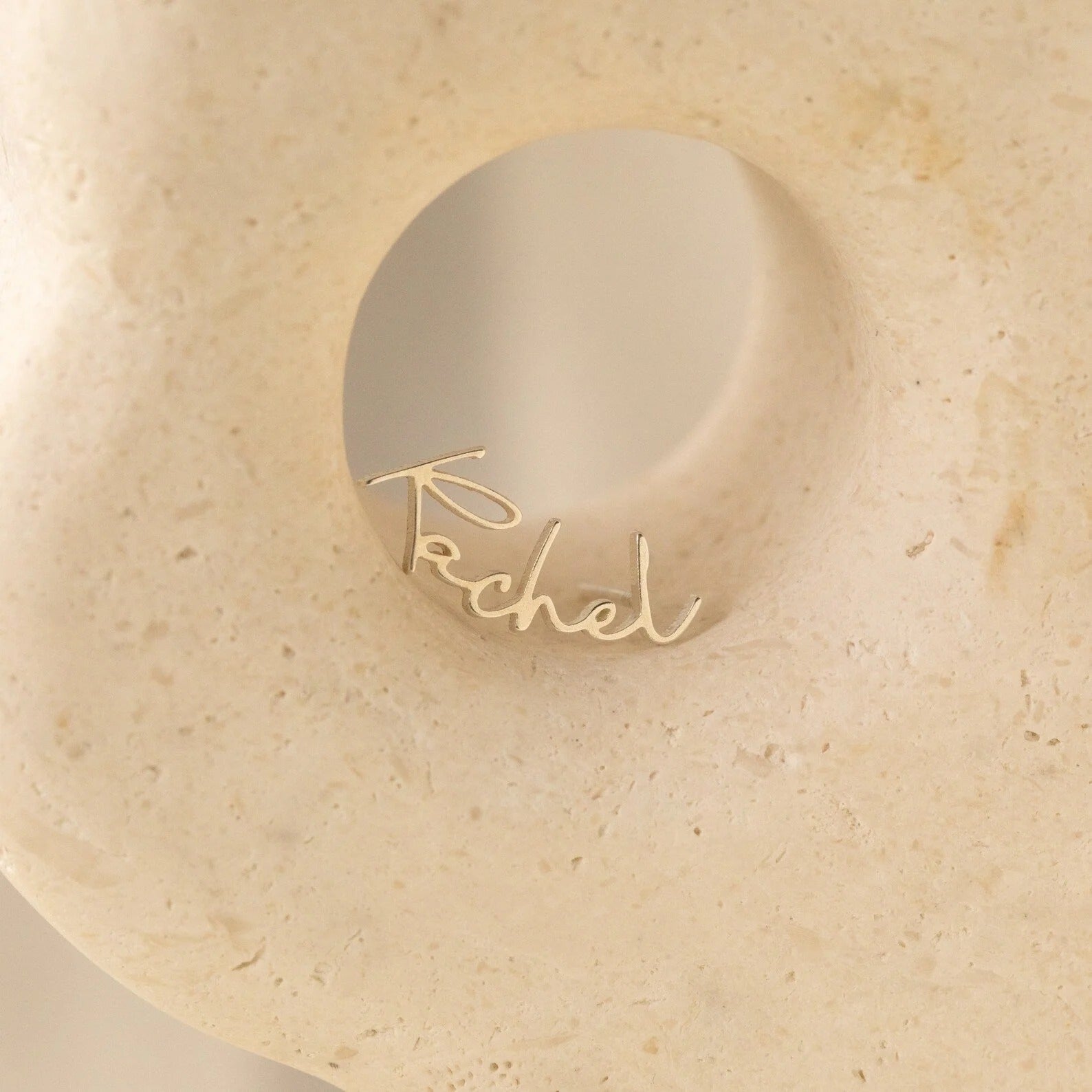 Gold ring with 'Rachel' engraving on a beige stone surface