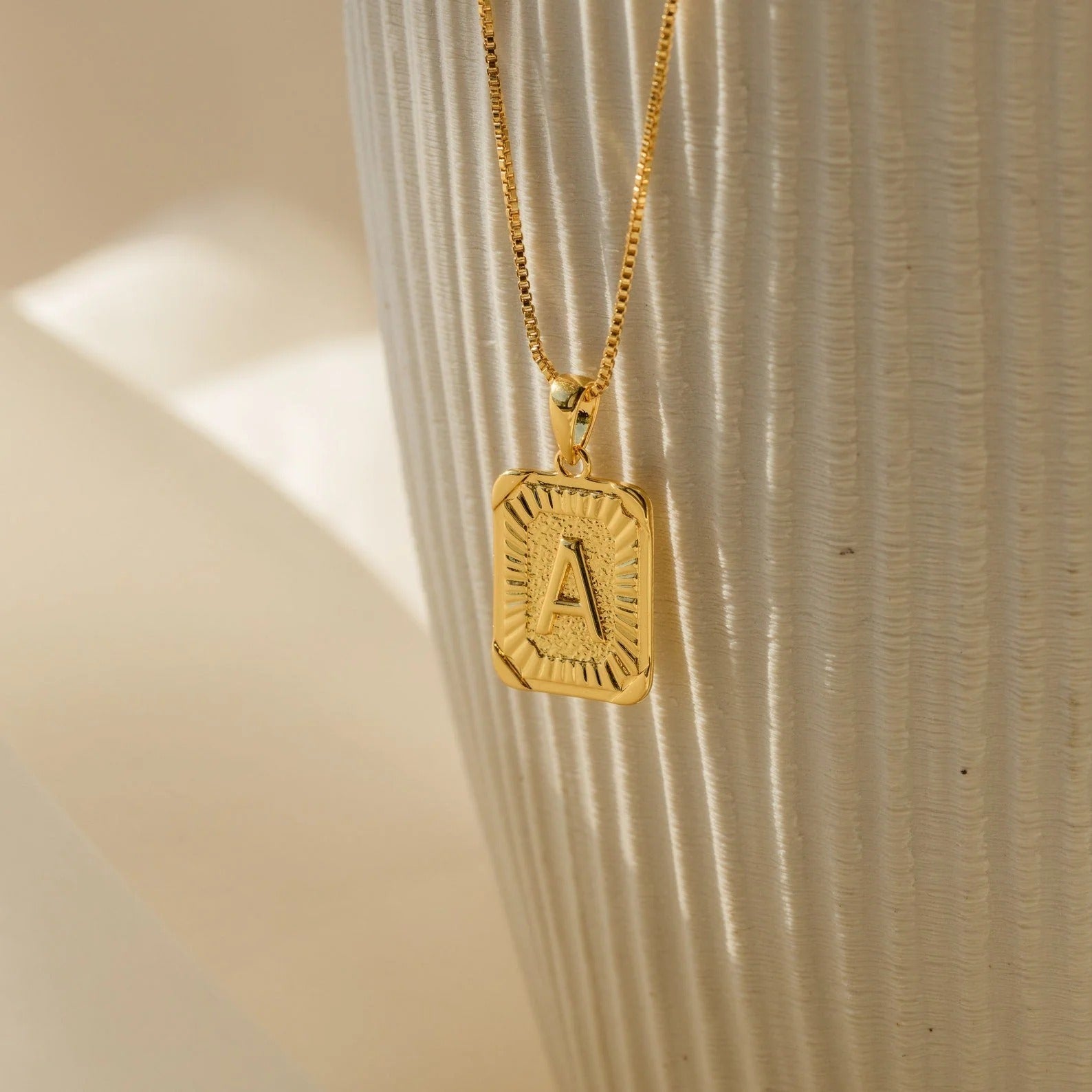 Gold necklace with a pendant featuring the letter 'A' on a textured beige background