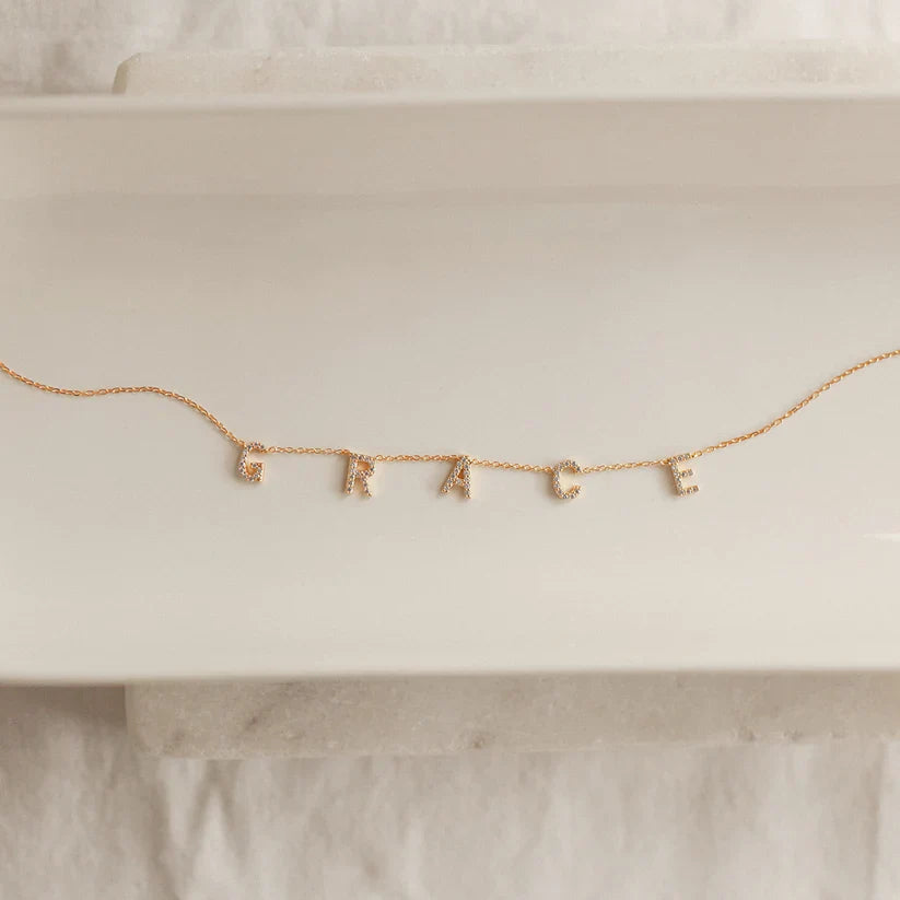 Gold necklace with letter charms spelling 'FAKE' on a white surface