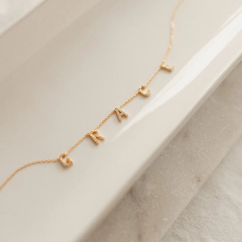 Gold necklace with letter charms on a light surface