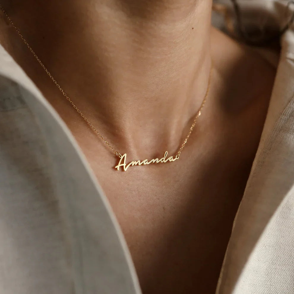 Gold necklace with 'Amanda' pendant on a person wearing a light-colored shirt.
