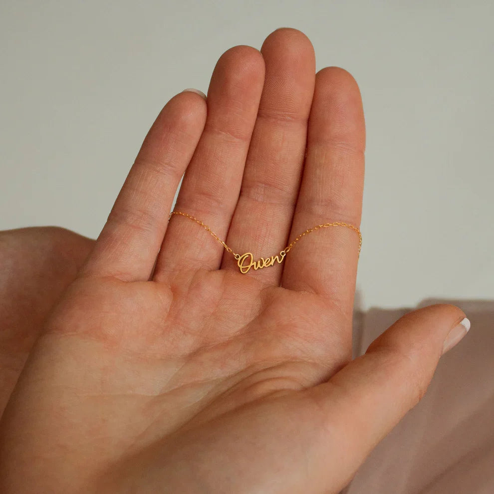 Gold necklace with 'Owen' pendant held in a hand against a neutral background