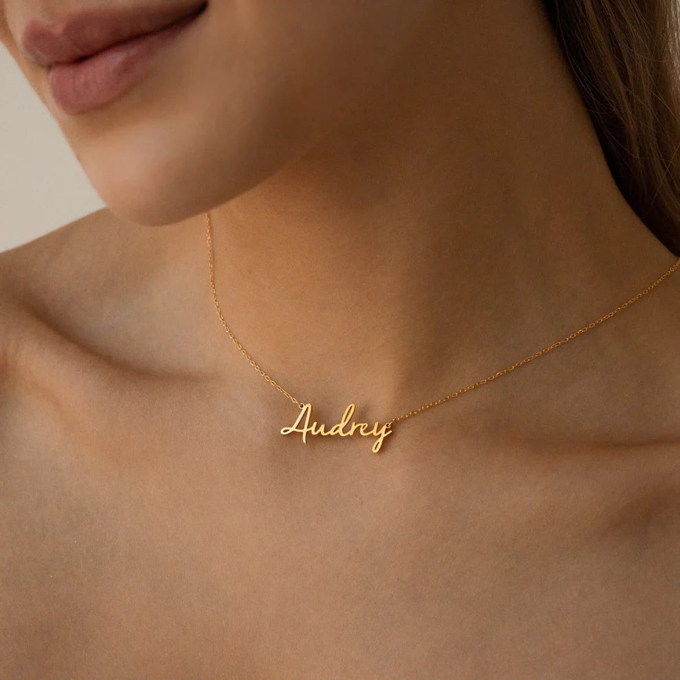 Gold necklace with 'Audrey' pendant on a person's neck against a neutral background