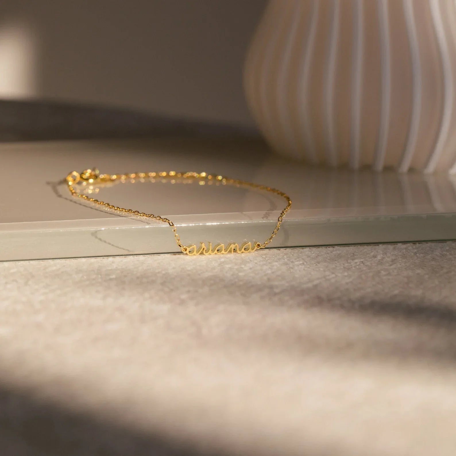 Gold bracelet on a light surface with a blurred vase in the background