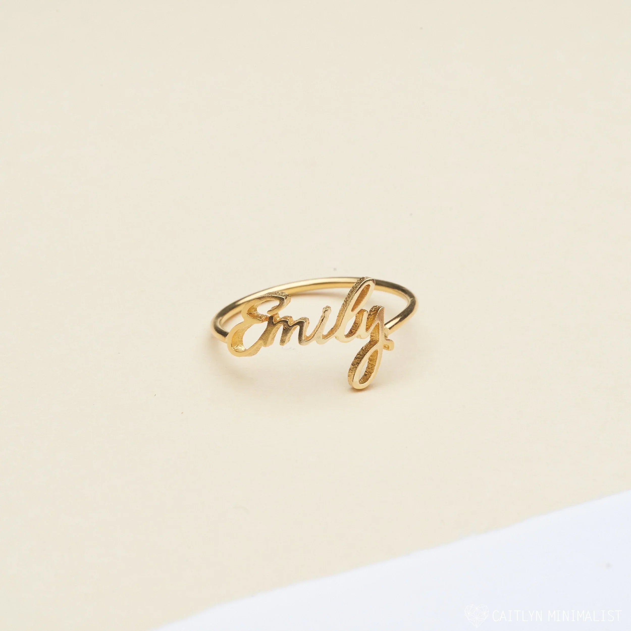 Gold ring with 'Emily' engraving on a beige background